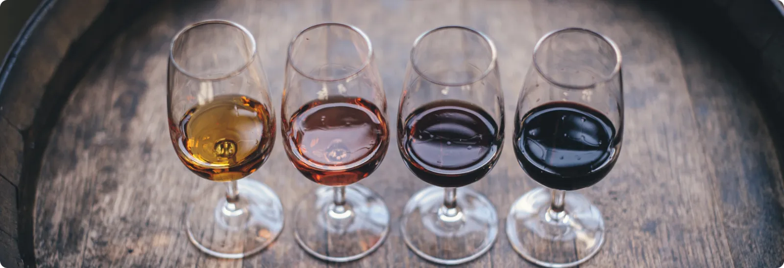 Four wine tasting glasses on a wooden barrel showing different wine colours